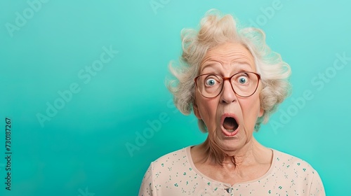 Shocked emotional elderly woman wearing glasses against blue studio background. Emotional expressions senior emotions