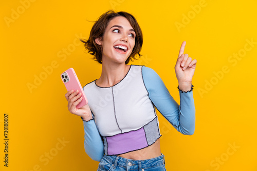 Photo of pretty positive woman wear top typing modern device looking pointing empty space isolated yellow color background
