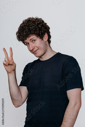 Wallpaper Mural Young Caucasian man wearing a black t-shirt on a white background making a peace gesture, pursing his lips and showing a V sign. Torontodigital.ca