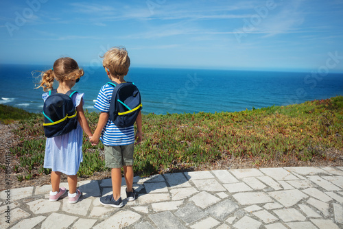 Boy and girl with backpacks admire sea from hill on summer