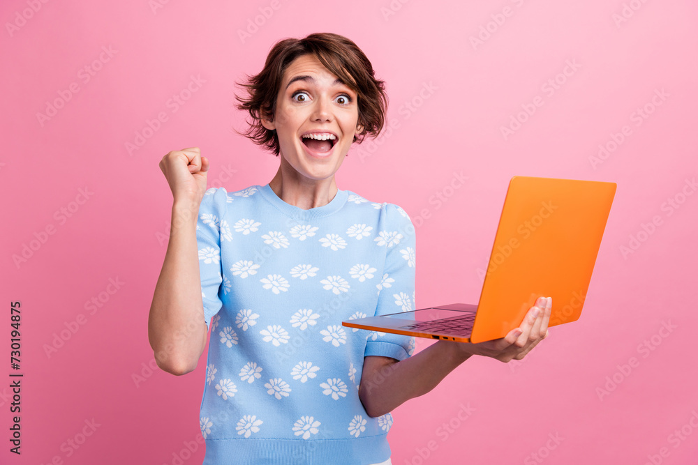 Portrait of delighted cheerful girl raise fist success achieve hold wireless netbook isolated on pink color background Portrait of delighted cheerful girl raise fist success achieve hold wireless netbook isolated on pink color background