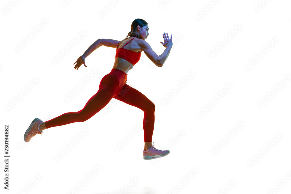 Competitive, concentrated young woman, runner, athlete in motion training, running over white studio background in neon light. Concept of sport, active and healthy lifestyle, sportswear, competition