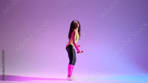 Lively girl from the 80s, dressed in sporty retro attire, brings energy to aerobics routine. Against a vivid purple backdrop, she seamlessly using dumbbells for a dynamic and fun workout. photo