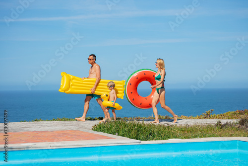 Two adults and a child, carry swim rings, walk by summer pool
