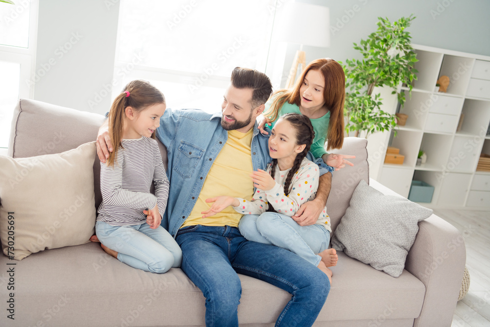 Portrait of four people positive guy embrace adorable girls sit on sofa speak communicating home indoors