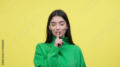 Happy Caucasian young woman playfully shows shush gesture with finger on lips on yellow background. Keeping gossips and secrets, provides silence or secrecy. photo