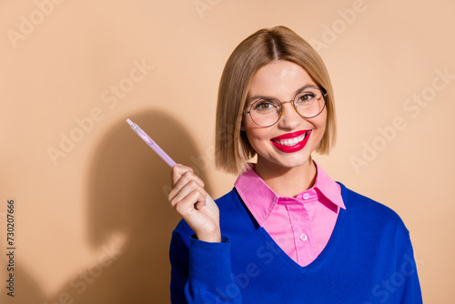 Fototapeta Naklejka Na Ścianę i Meble -  Photo of positive lovely person toothy smile hold point pen empty space offer isolated on beige color background