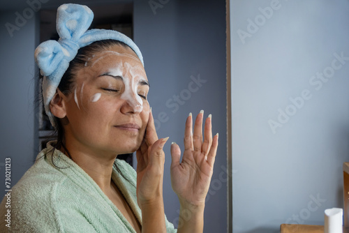 Latin girl applies cleansing foam on her face.