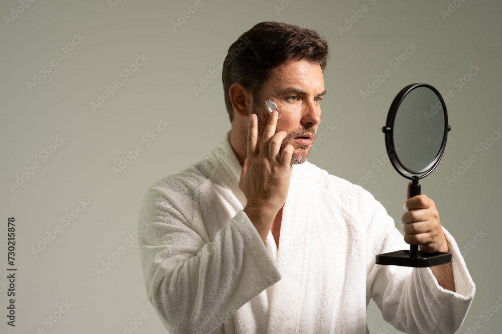 Smiling man look in bath mirror apply after shave balm on healthy face. Cosmetic cream for man. Spa male model, skincare product for skin face. Morning mask for skin with anti-aging effect. Skin care. Smiling man look in bath mirror apply after shave balm on healthy face. Cosmetic cream for man. Spa male model, skincare product for skin face. Morning mask for skin with anti-aging effect. Skin care.