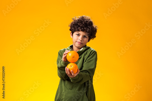 Child boy holding orange fruits over yellow background. Healthy food concept