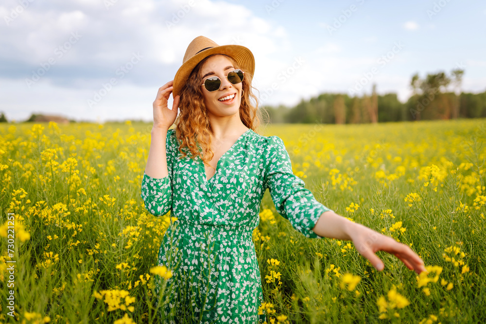 Fototapeta premium Beautiful woman walking in the blooming field at sunny summer day. Nature, vacation, relax and lifestyle. Summer landscape.