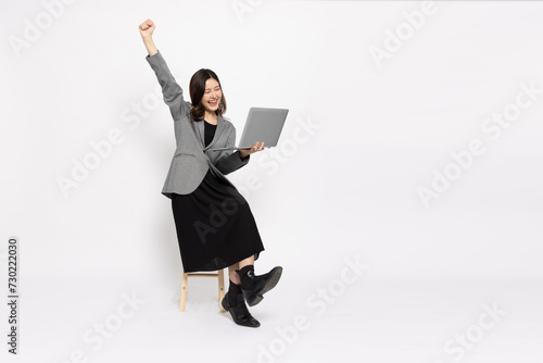 Happy young Asian businesswoman using laptop computer and sitting on wood chair isolated on white background