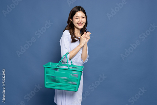 Asian businesswoman smiling and holding grocery basket isolated on blue background, Shopping and Supermarket concept