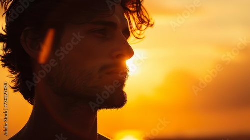 Portrait shot of handsome brunette man with beard sitting outdoor in the fields looking at camera at sunset