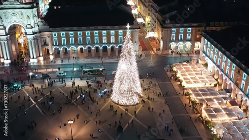 Aerial drone shot of Commerce Square illuminated and decorated at Christmas time in Lisbon night, Christmas tree and people tourists crowd around, city of Europe