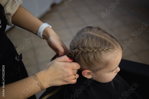barber in a hairdressing salon braids pigtails to a little cute girl