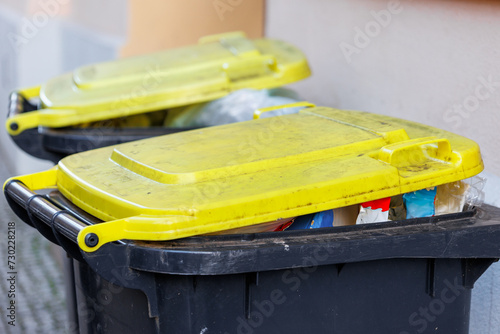 Full recycling plastic yellow packing bins with yellow lids against an urban backdrop, signaling waste management photo