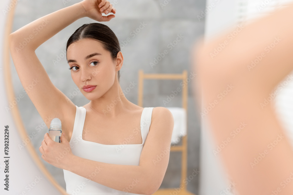 Beautiful woman applying deodorant near mirror in bathroom Beautiful woman applying deodorant near mirror in bathroom