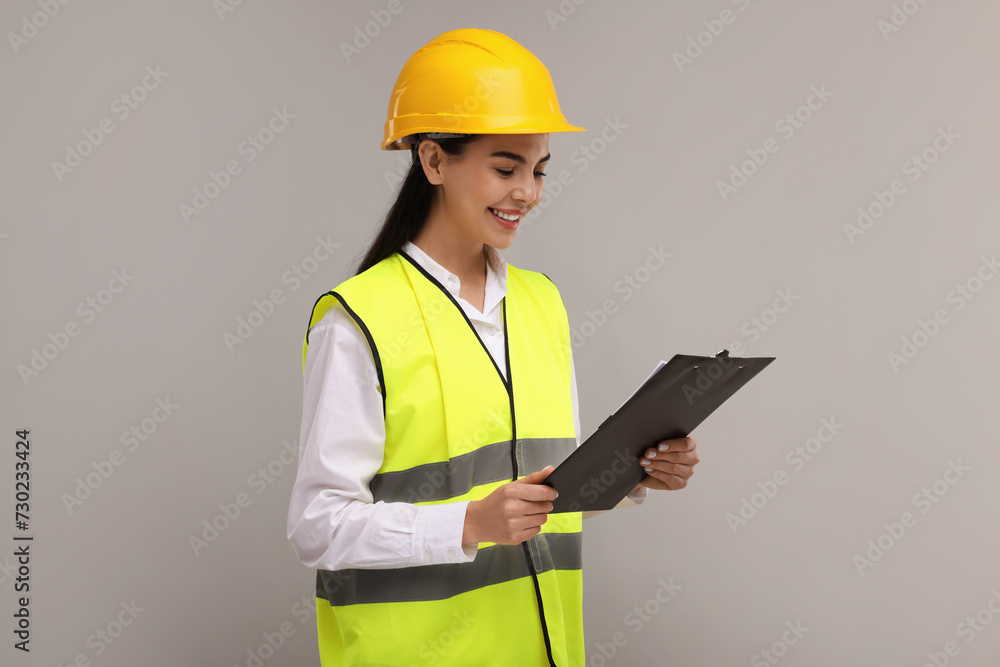 Engineer in hard hat holding clipboard on grey background Engineer in hard hat holding clipboard on grey background