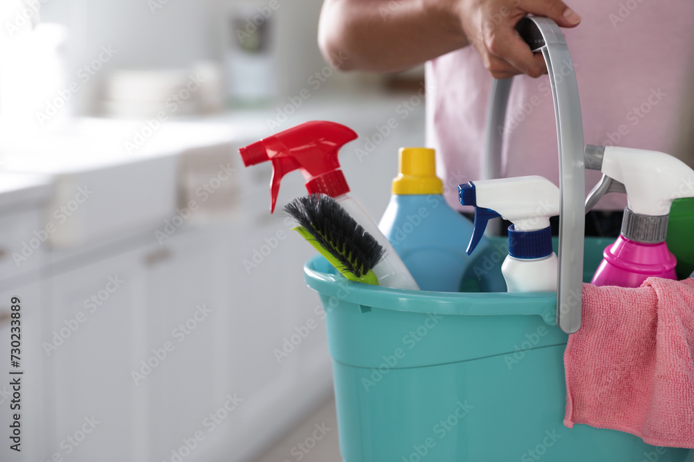 Woman holding bucket with cleaning supplies in kitchen, closeup. Space for text