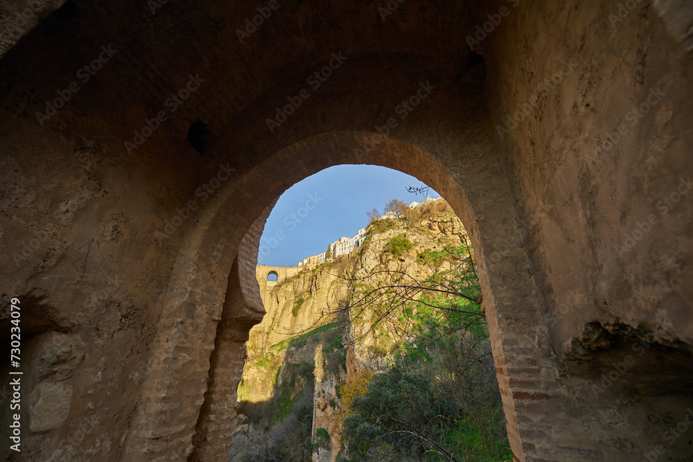 View of the new bridge of the village of Ronda through the old destroyed arch in the rays of the setting sun