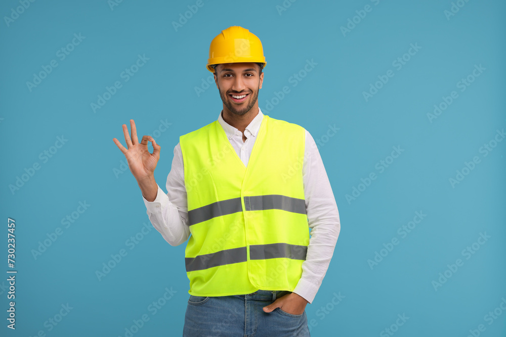 Engineer in hard hat showing ok gesture on light blue background