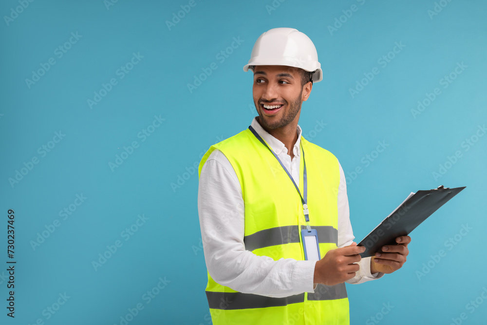 Engineer in hard hat holding clipboard on light blue background, space for text Engineer in hard hat holding clipboard on light blue background, space for text