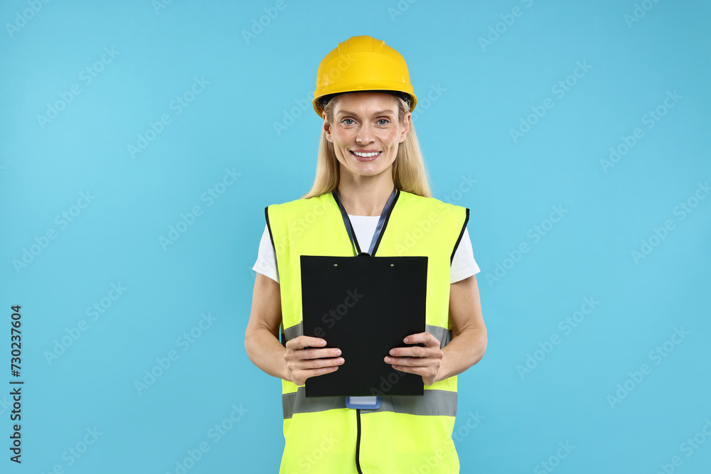 Engineer in hard hat holding clipboard on light blue background Engineer in hard hat holding clipboard on light blue background