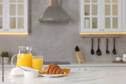 Breakfast served in kitchen. Fresh croissant, jam, honey and orange juice on white table. Space for text photo