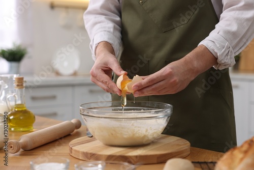 Making bread. Man putting raw egg into dough at wooden table in kitchen, closeup
