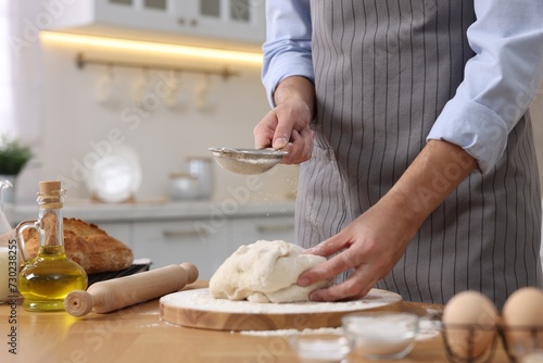 Making bread. Man sprinkling flour onto dough at wooden table in kitchen, closeup