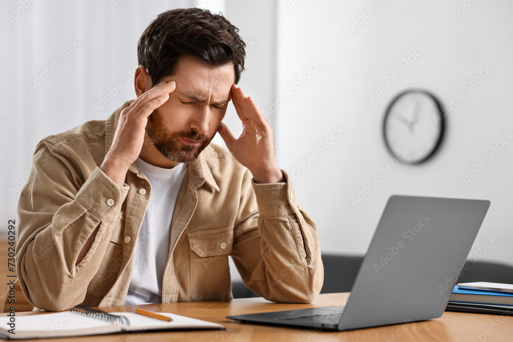 Tired man suffering from headache at workplace in office Tired man suffering from headache at workplace in office