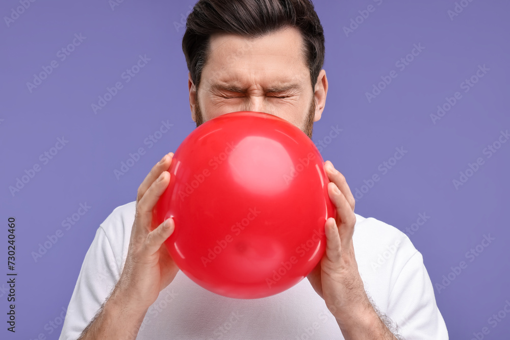 Man inflating red balloon on purple background Man inflating red balloon on purple background