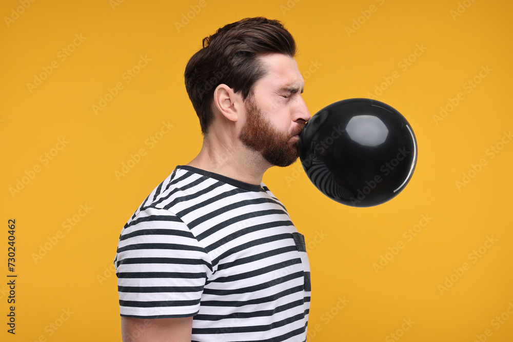 Man inflating black balloon on yellow background Man inflating black balloon on yellow background