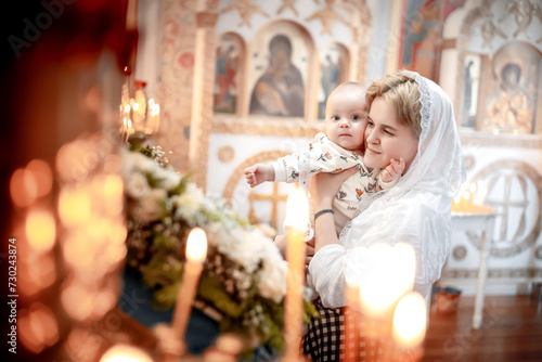 a mother with a small child in an Orthodox Christian church or temple prays or came to the sacrament of baptism, believers in a holy place at the altar or icons photo