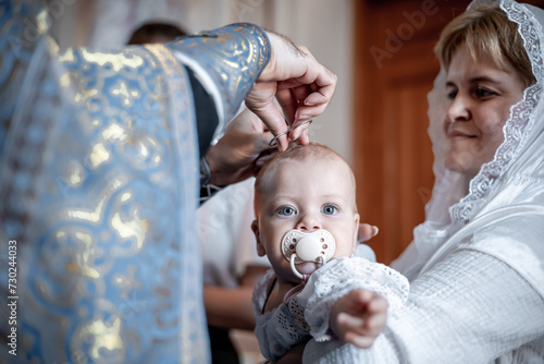 cutting or clipping hair with scissors by a small child in an Orthodox Christian church or temple during the sacrament of baptism with a priest or clergyman photo