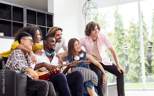 Group of diverse friends or people wearing casual clothes  relax smiling with happiness  party celebration  sitting in living room at cozy home  playing guitar and singing. Birthday  New Year Concept.