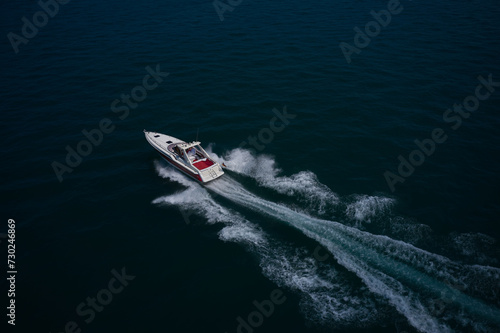 A large red-white boat moves quickly on blue water, moving diagonally, top view. A large boat with people moving on the water, aerial view.