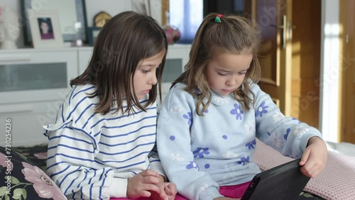 Two sisters looking at a tablet, sitting on a camera. Concept of play, learning, having fun, sharing, together and twins.