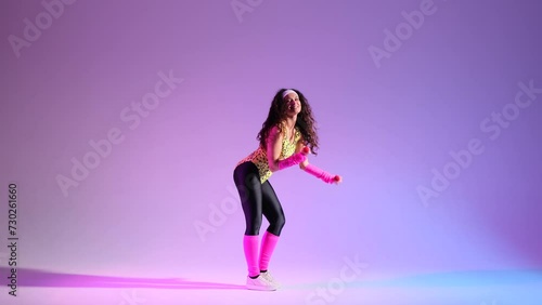 Against a purple backdrop, cheerful girl in a lively 80s aerobics session. With a smile, she using dumbbells, bringing a retro flair to energetic workout. photo