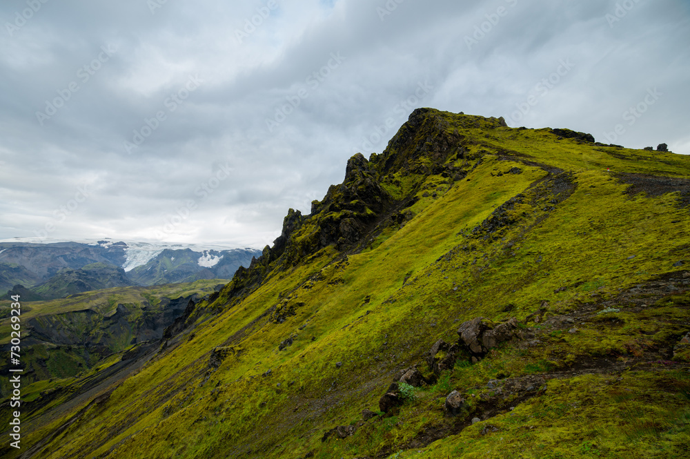 The picturesque pass on a rock in a famous Laugavegur hiking trail. Icelandic landscape of volcanic rhyolite mountains in cloudy weather with colourful grass. Iceland in august. Horizontal crop