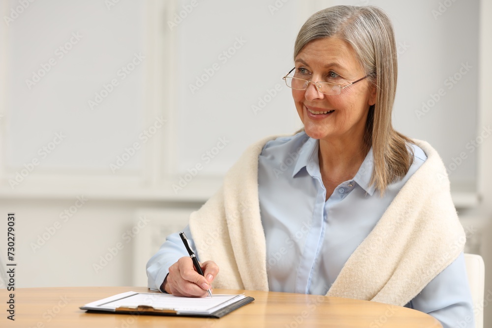 Smiling senior woman signing Last Will and Testament at table indoors. Space for text Smiling senior woman signing Last Will and Testament at table indoors. Space for text