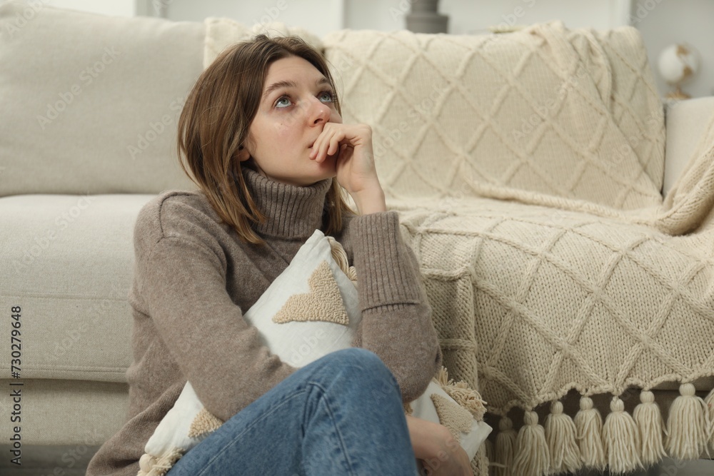 Sad young woman sitting near sofa at home Sad young woman sitting near sofa at home