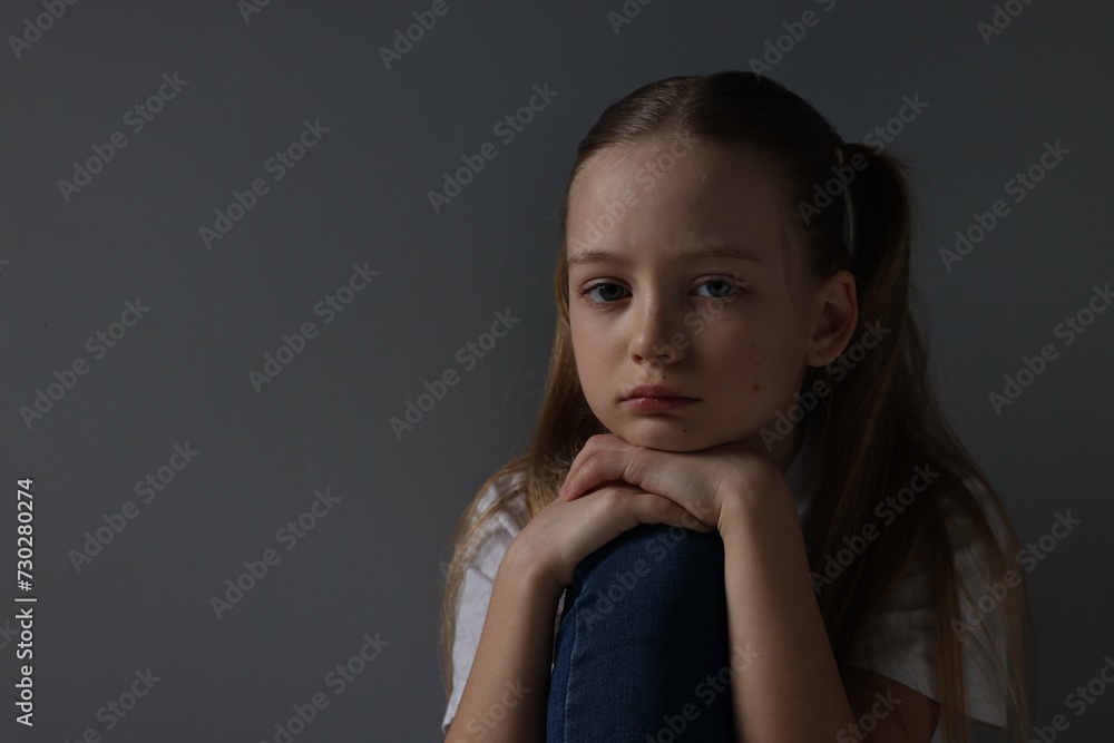 Sad girl sitting near dark grey background, space for text Sad girl sitting near dark grey background, space for text