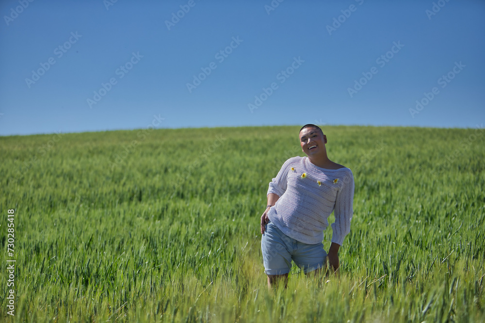 Young, South American, non-binary person, heavily makeup, posing in a white sweater with natural daisies, in the middle of a green wheat field, smiling and happy. Concept queen, lgbtq+, pride, queer.