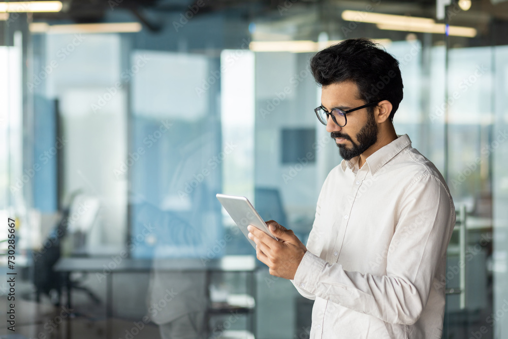 Focused indian businessman with beard using tablet in modern office space Focused indian businessman with beard using tablet in modern office space
