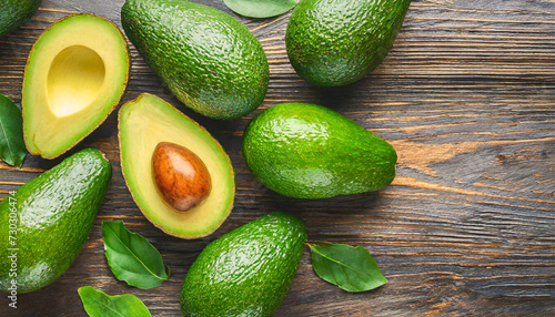 Whole and cut avocados on wooden background.