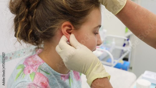 Doctor hand wipes ear with sterilizing solution before piercing to teenage girl photo