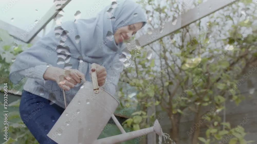 Animation of water drops over biracial woman in hijab with watering can, gardening Animation of water drops over biracial woman in hijab with watering can, gardening