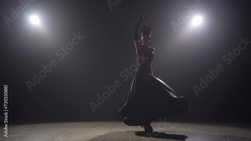 Woman dancing on black background under spotlights. Spanish dancer in red-black dress dancing elements of passionate flamenco.